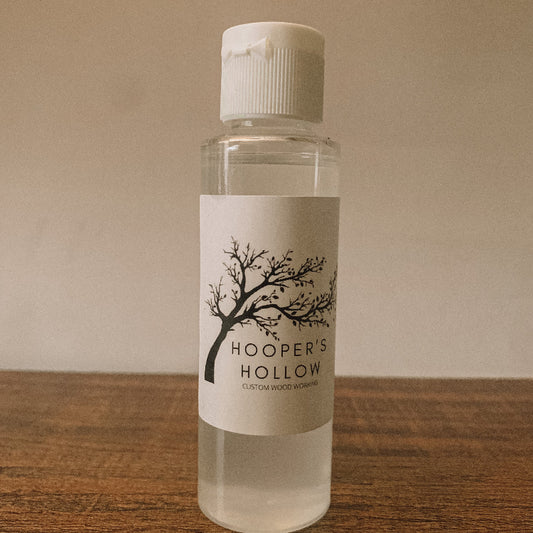 Clear plastic bottle of Hooper's Hollow custom wood finishing product stands on a wooden table.